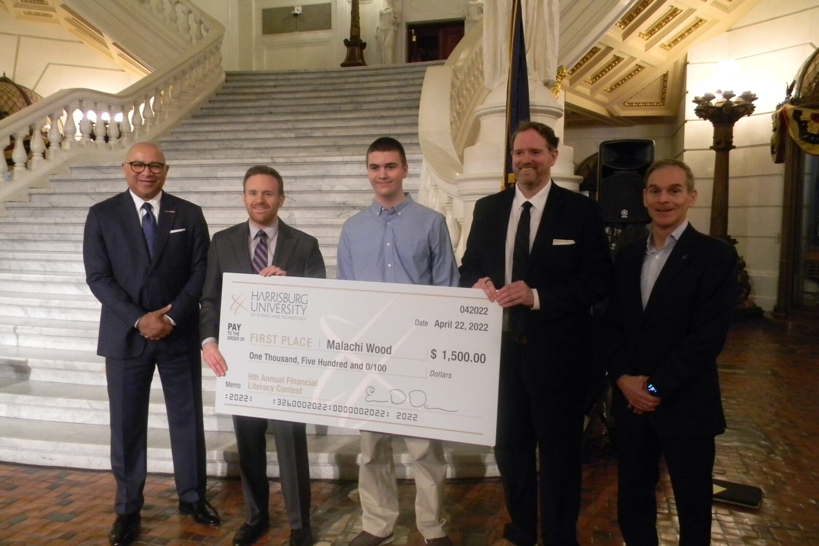 First-place winner Malachi Wood poses with Harrisburg University representatives while holding a $1,500 award check for the Statewide Student Financial Literacy Competition